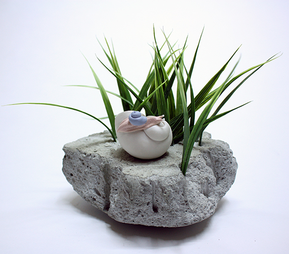 BETHANY_KRULL_RemnantofExtinction_snailstudy Rock with grass and small ceramic object.