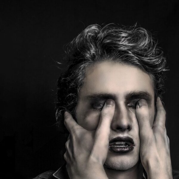 black and white closeup of young man with thumbs digging into his eyes