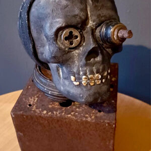 A skull with a metal face on top of a wooden block.