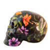 A black skull with flowers and a hummingbird painted on it.